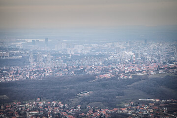Fototapeta premium Winter panorama of Belgrade, Serbia, seen from above under dense smog and haze. Reduced visibility across residential districts and the distant skyline highlights winter urban air pollution.