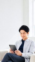 Fototapeta premium 自宅のソファでくつろぎながらタブレットを見る男性