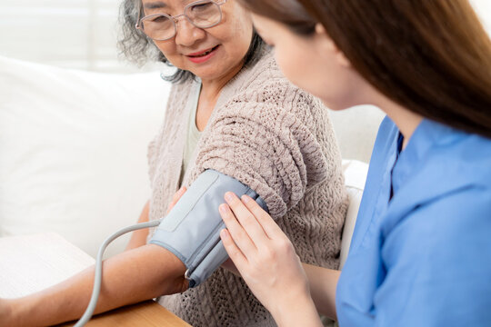 Asian woman nurse measuring blood pressure senior patient, medical checking for hypertension monitoring, caregiver support elderly woman with arterial blood pressure device, routine health checkup.