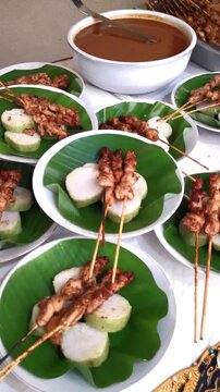 Vertical pan over catered plates of Indonesian traditional chicken satay sate ayam with rice cakes on banana leaves