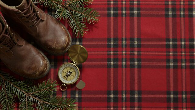 Brown boots, compasses, pine branches on red plaid fabric.