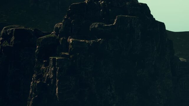 The scene shows rugged cliffs rising sharply under the sky during the late afternoon. The rocks appear weathered and rough, casting shadows on the ground below.