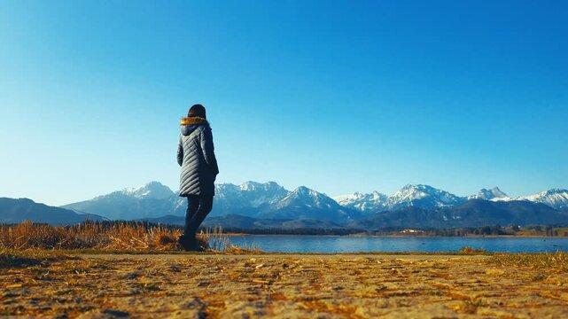 Woman admiring snow-covered Bavarian Alps beside a peaceful alpine lake near F&uuml;ssen, Germany. Scenic winter travel and nature landscape in Europe.