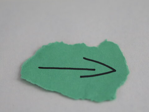 Una flecha de color verde en un papel rasgado en un fondo blanco 
