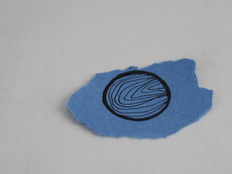 Un papel rasgado de color azul con una figura de un circulo con muchas rayas por dentro en un fondo blanco
