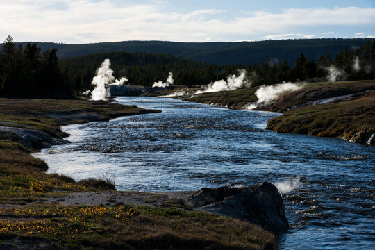 Evening walk through the upper gyser basin, fumaroles on Firehole river with hot steam rising, summer tourism at Yellowstone National Park viewing natural geothermal features
