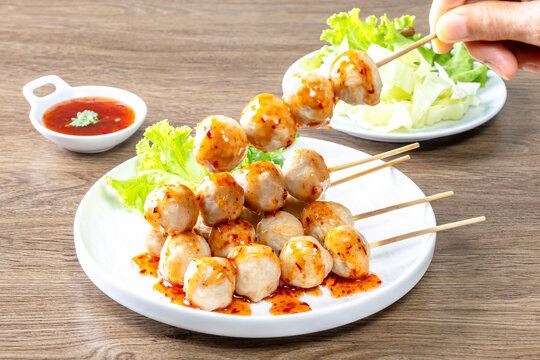 Thai grilled meatballs with sweet and spicy dipping sauce, served on a white plate (Thai street food).