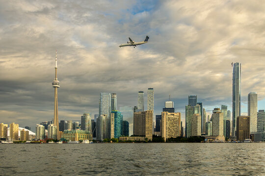 Turboprop aircraft flying over Toronto's Inner Harbour skyline at dawn with dramatic clouds in August