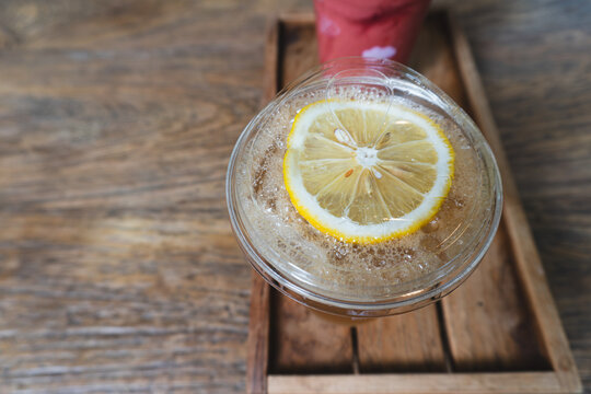 Top down close up view of a refreshing iced lemon tea in a clear plastic takeaway cup on a wooden tray