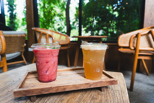 Refreshing berry smoothie and iced lemon tea on a wooden tray in a cozy cafe with a green nature view