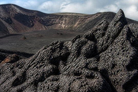 Porous black volcanic scoria at a crater's edge, textured surface.