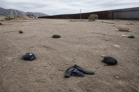 Empty border fence area with abandoned backpacks and folded jacket, migration and displacement concept