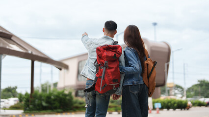 Obraz premium Rear view of Asian couple backpackers pointing at destination during outdoor travel