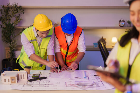Asian engineers measuring architectural blueprints with compass on office desk