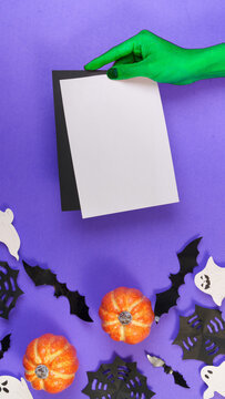 Green witch hand holding blank card mockup over purple Halloween background