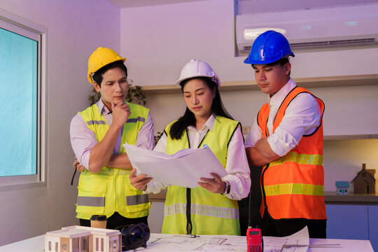 Asian architectural team reviewing floor plan blueprints in modern office