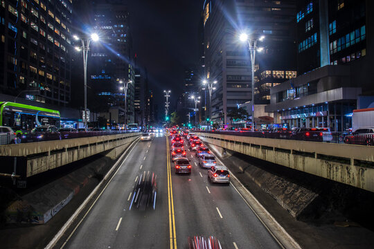 Night view of Paulista Avenue with long exposure vehicle light trails rushing through the tunnel underpass surrounded by illuminated skyscrapers and urban architecture in the financial center.