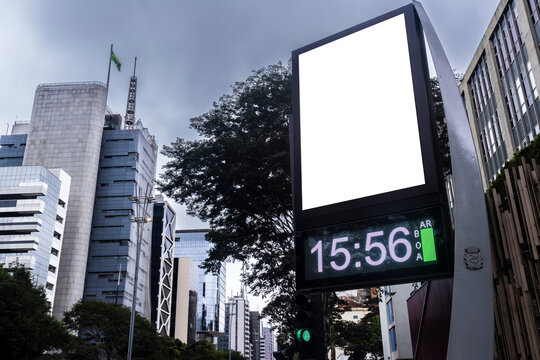 Digital billboard with blank white mockup display on Paulista Avenue. A modern street clock with an isolated white screen frame for advertisement placement, 