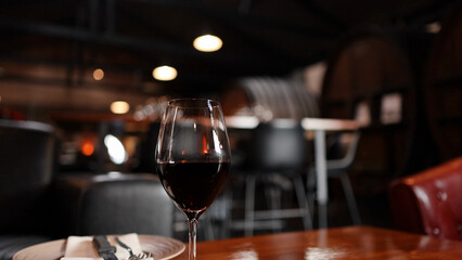 Fototapeta premium Glass of Red Wine on Wooden Table in Rustic Cellar