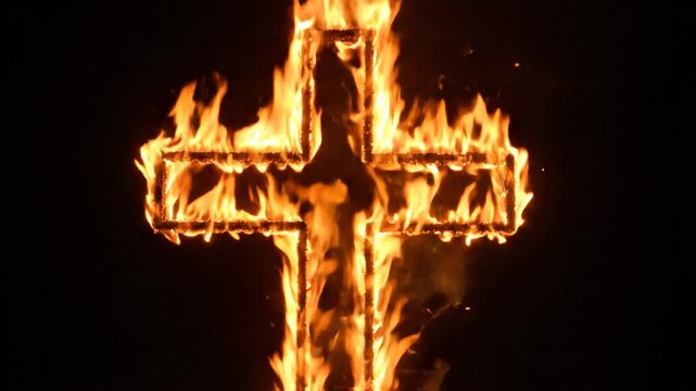 Burning Christian cross symbol engulfed in bright orange flames at night.