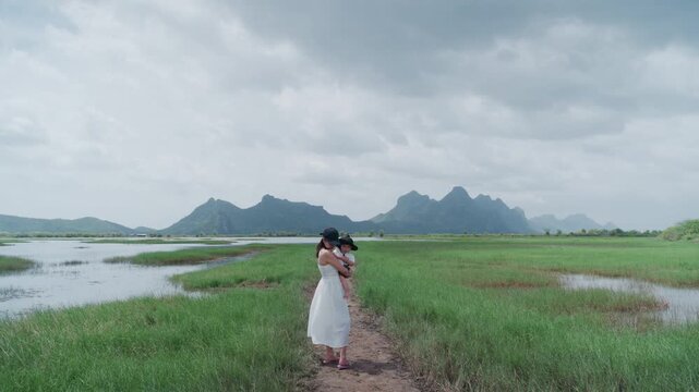 4K Asian young woman holding baby in arms standing outdoors in nature during family trip.