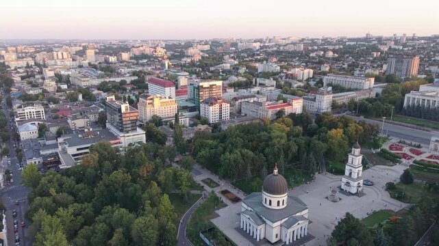Cinematic drone pullback over central Chisinau, Moldova, revealing the Nativity Cathedral, bell tower, Triumphal Arch, Cathedral Park and an expansive capital city skyline. Historic landmarks, green u