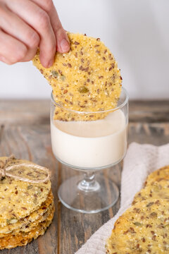 Home pastry. Grain biscuits. Woman hand plunging superfood flax seeds baked cookies in white liquid glass on wooden kitchen countertop.