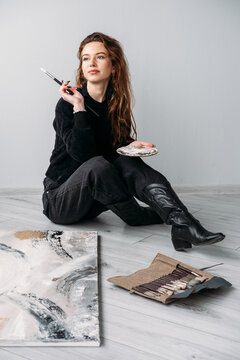 Painter studio. Female artist. Inspired creative woman with brush ink palette using canvas on floor at professional workplace.