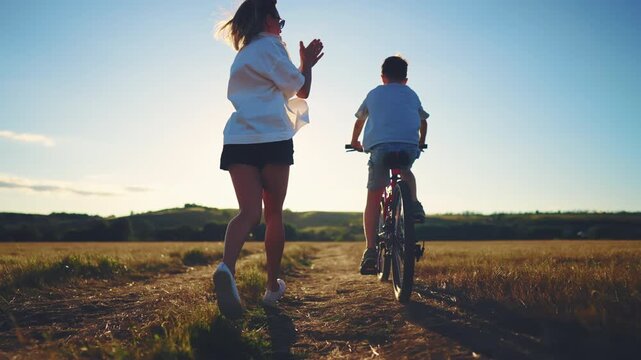 Mother love and support, woman teaching little boy to ride bicycle, back view. Summer vacation in countryside, child and mom feeling happiness and joy, family time in summer holidays, childhood