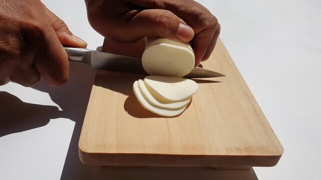 Cutting raw cassava on a wooden chopping board.