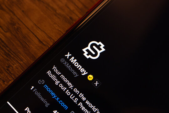 Mexico City, MEXICO - Jul 28 2026 : Close-up of a smartphone on a wooden table showing the verified @XMoney profile on X, with its logo and a bio announcing the rollout to U.S. Premium subscribers.