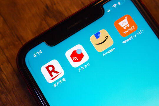 Mexico City, MEXICO - Jul 28 2026 : Close-up of an iPhone home screen on a wooden table showing shopping app icons for Rakuten Ichiba, Mercari, Amazon, and Yahoo Shopping against a turquoise wallpaper