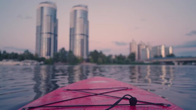 Close Up of Bungee Cords on Red Paddleboard with Blurred City Skyline | Shallow Depth of Field Rotating SUP Board Deck Detail | Waterfront Sunset Equipment