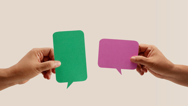 Two hands hold colorful blank speech bubbles over a neutral background, symbolizing communication, dialogue