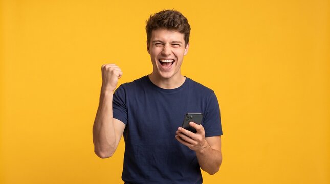 Excited young man celebrating victory holding smartphone over yellow background