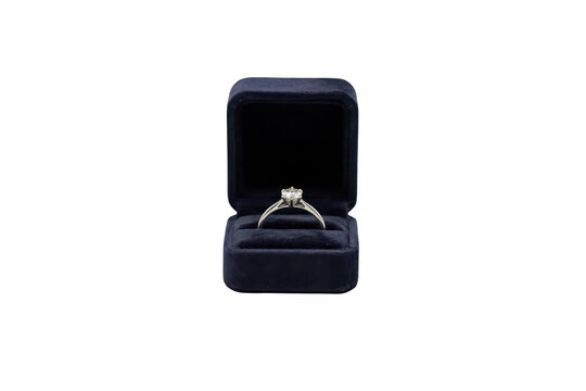 A classic solitaire diamond engagement ring with a silver band, resting inside a dark blue velvet jewelry case against a solid black background