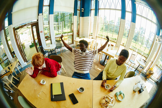 Diverse group of people working in cafe, African American man celebrating success with raised arms. Image ideal for youth lifestyle, education, and peer collaboration marketing