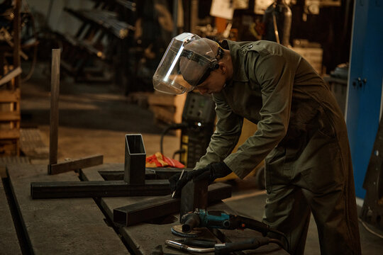 Young adult Caucasian male welder wearing protective face shield measuring metal parts in workshop. Image suitable for industrial manufacturing and vocational training promotions