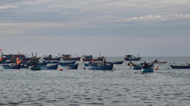 Traditional fishing boats and coracles anchored off the coast at sunrise after transferring fresh fish catch to beach market in early morning