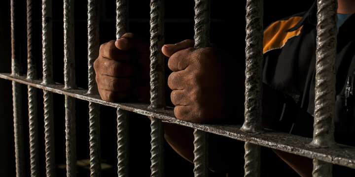 prisoner's hands behind bars with black background