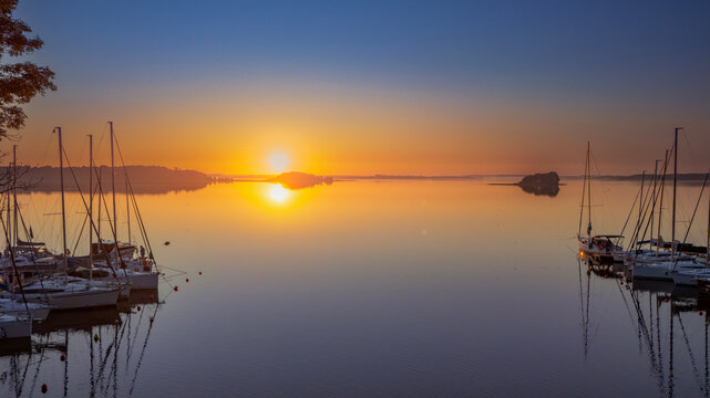 Golden sunrise reflecting over calm lake with docked sailboats