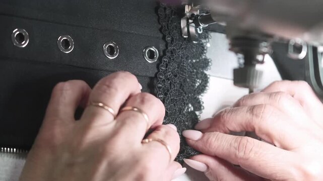 Vertical video. Professional sewing. Garment making. Tailor hands decorating black corset with lace. Precision needle work on electric stitching machine.