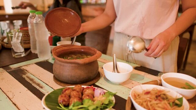 Woman Serving Traditional Thai Isan Cuisine from Clay Pot