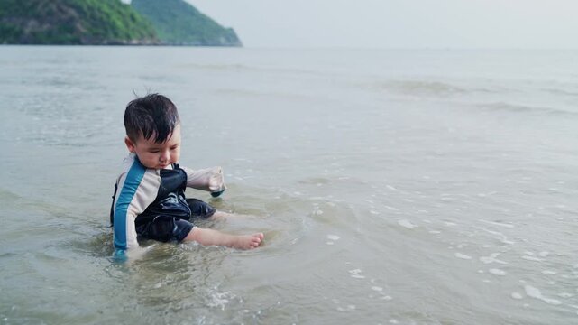 Cute Toddler Playing in Sea Water on the Beach with Mountain Background