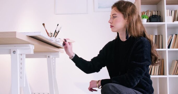 Artist studio. Talented painter. Female master using brush working on wooden table at professional art workplace indoor.