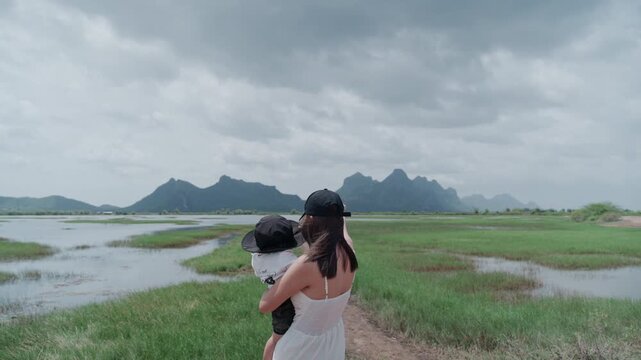 4K Asian young woman holding baby in arms standing outdoors in nature during family trip.