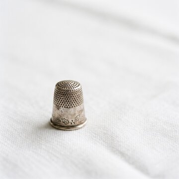 Vintage silver thimble with detailed floral engraving resting on white linen fabric background, macro view.