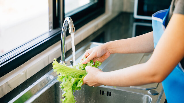 Fresh vegetables being washed by a woman's hand under running water in a modern kitchen sink preparing for a vegan salad. Hygiene and freshness in homemade healthy food preparation.