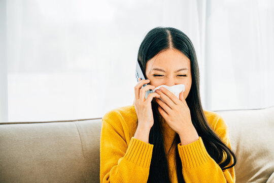 Sick woman seated on sofa contacts doctor blowing wiping nose sneezing. An ill young girl consults practitioner on phone about flu symptoms seeking medicine. Illustrating patient care at home.