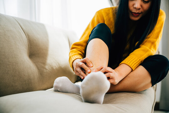 Health care concept showcased, a woman seated on a sofa massaging her painful foot with a red-highlighted area. Illustrating recovery reflexology and relief from discomfort.